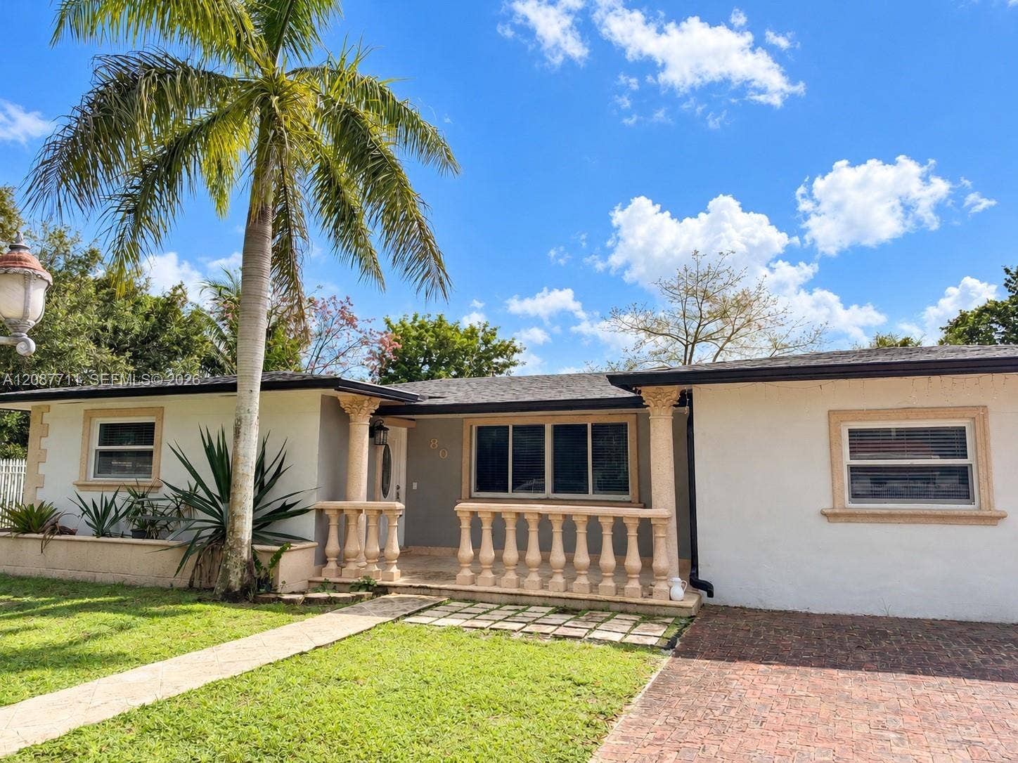 80 NE 162nd Street, Miami, Miami, FL 33162 Exterior facade featuring stucco siding, a stone-balustrade front porch, decorative pillars, and a brick-paved driveway