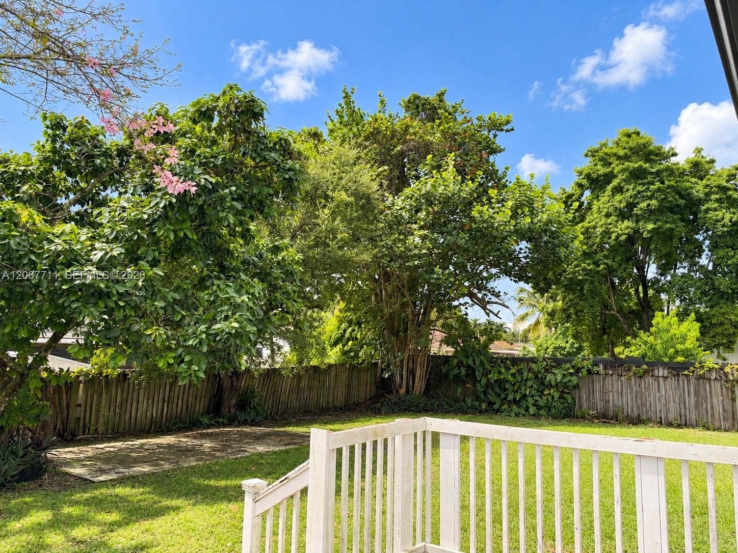 80 NE 162nd Street, Miami, Miami, FL 33162 Backyard featuring a wood deck with white railings, a concrete patio, perimeter wood fencing, and mature trees