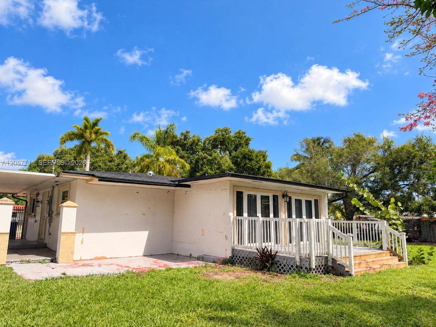 80 NE 162nd Street, Miami, Miami, FL 33162 Exterior featuring a raised deck with white railings, a concrete patio area, a covered carport, and multi-panel glass doors