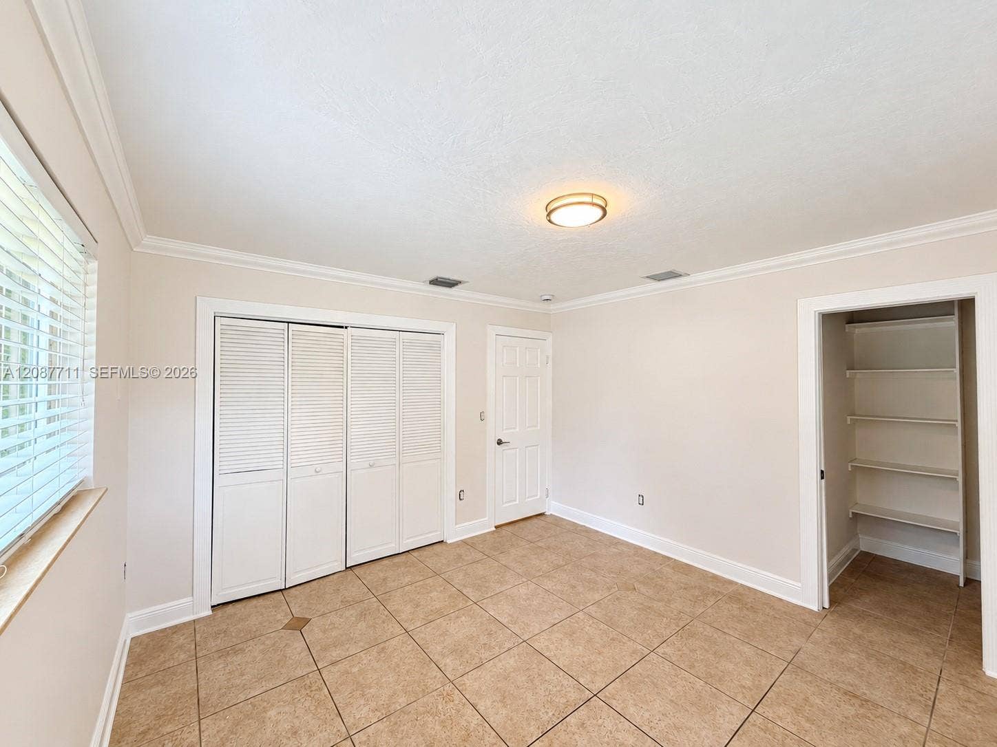80 NE 162nd Street, Miami, Miami, FL 33162 Room featuring tile flooring, crown molding, a multi-panel door, built-in louvered-style closet doors, and a reach-in storage area with fixed shelving