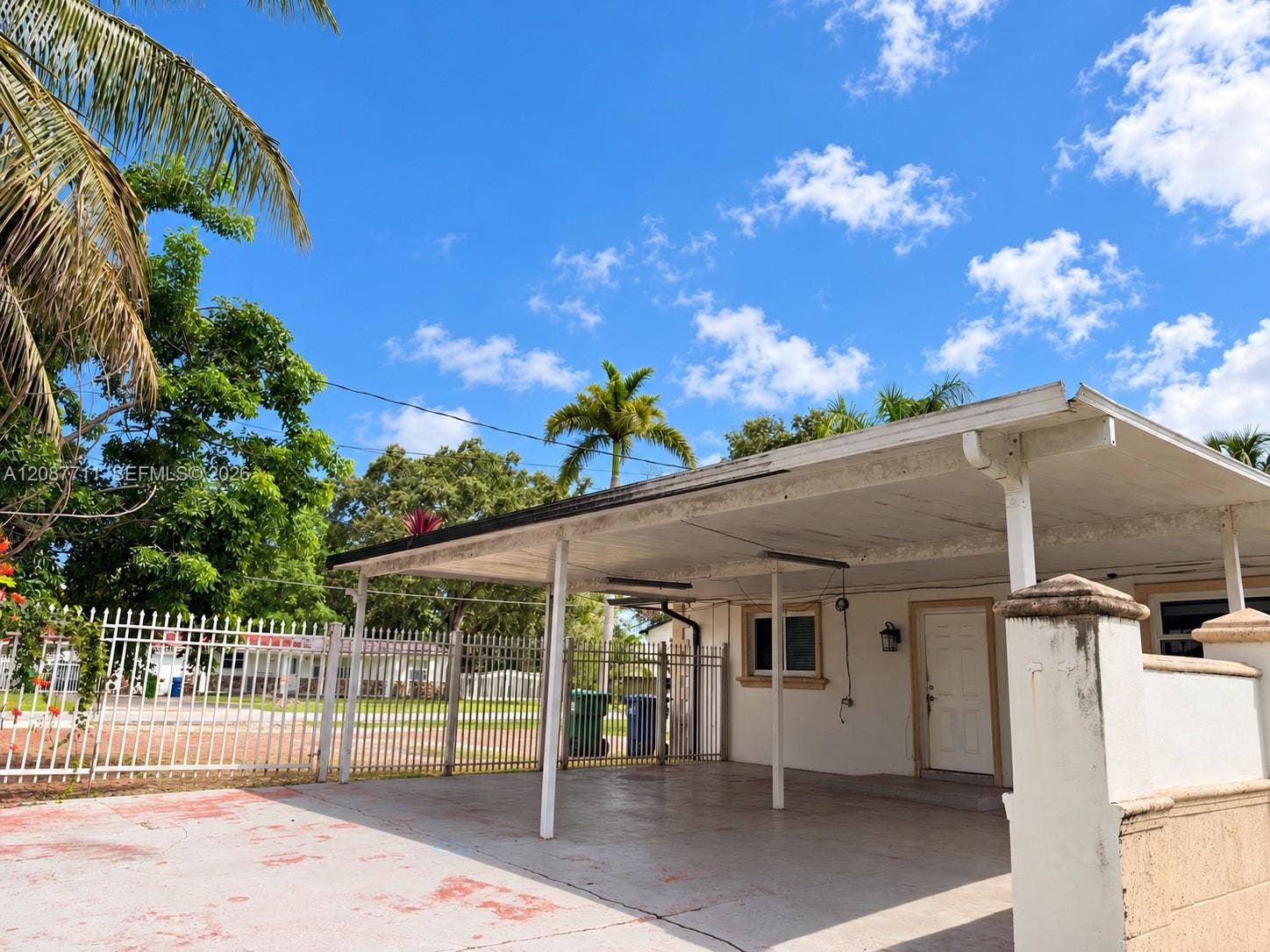 80 NE 162nd Street, Miami, Miami, FL 33162 Covered concrete carport with integrated support pillars, gated perimeter fencing, and concrete driveway surface