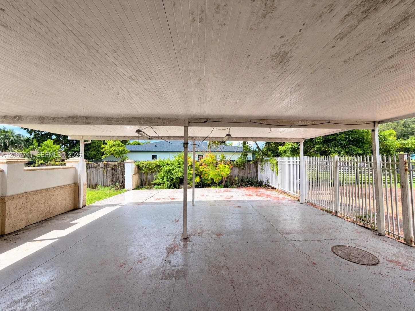 80 NE 162nd Street, Miami, Miami, FL 33162 Covered parking area featuring a concrete floor, structural metal support posts, and a white aluminum privacy fence