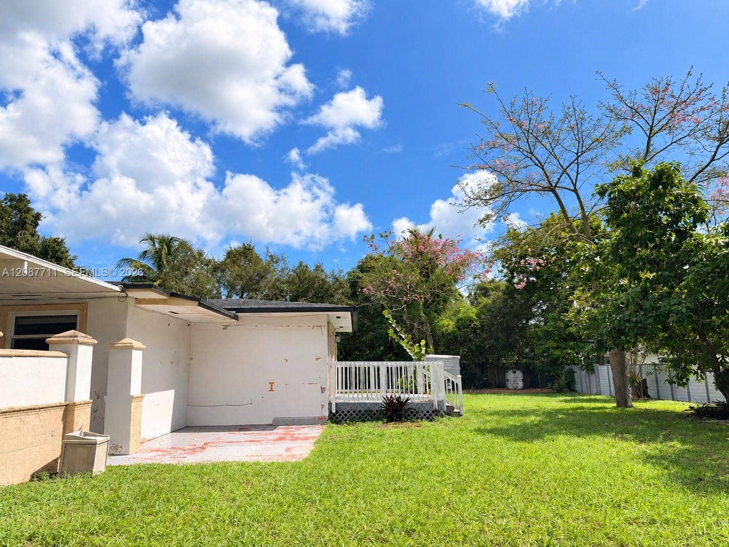 80 NE 162nd Street, Miami, Miami, FL 33162 Expansive backyard featuring a manicured lawn, white wood-slat deck, masonry perimeter fencing, and mature trees
