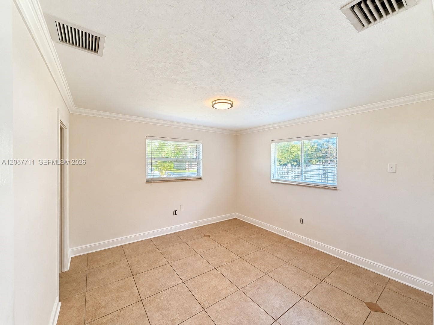 80 NE 162nd Street, Miami, Miami, FL 33162 Neutral-toned interior featuring large-format square tile flooring, crown molding, dual windows with horizontal blinds, and a centered flush-mount ceiling fixture