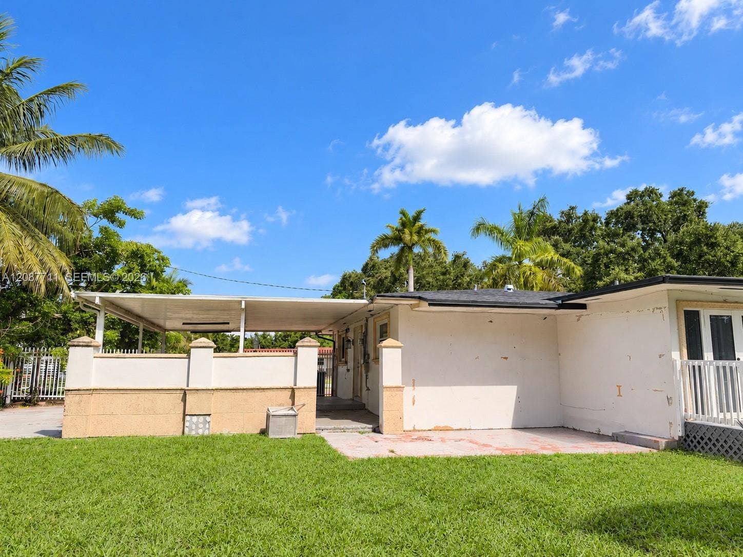80 NE 162nd Street, Miami, Miami, FL 33162 Rear exterior featuring a covered patio, stucco and masonry wall, integrated carport, concrete flooring, and manicured lawn