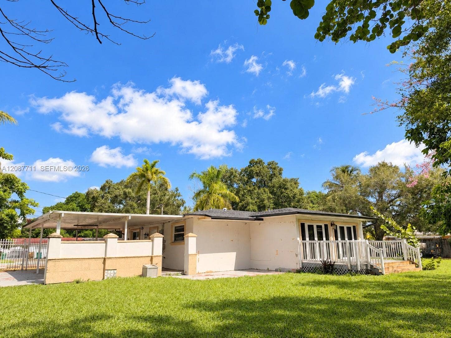 80 NE 162nd Street, Miami, Miami, FL 33162 Single-story residence featuring an attached carport, covered side porch with decorative pillars, white railing, and a spacious lawn