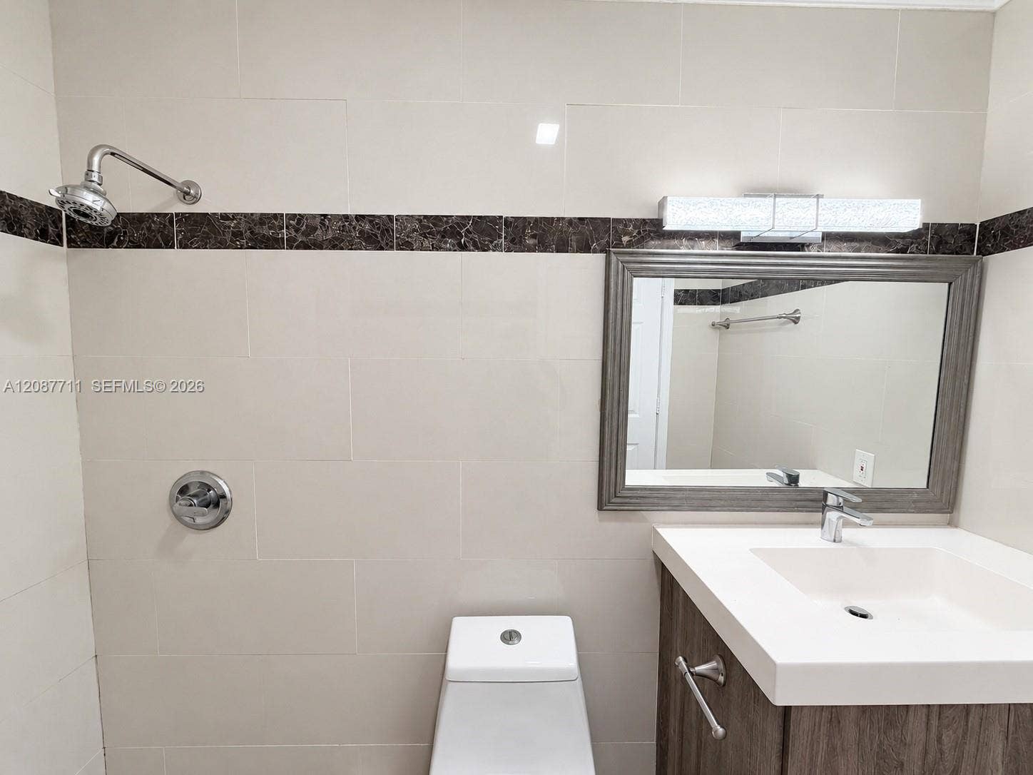 80 NE 162nd Street, Miami, Miami, FL 33162 Bathroom featuring floor-to-ceiling cream tiling with dark stone accent banding, a vanity with an integrated basin, wall-mounted brushed-metal hardware, and a linear light fixture