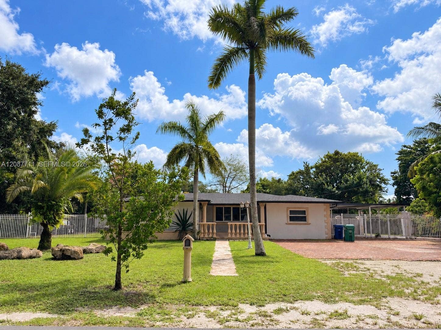 80 NE 162nd Street, Miami, Miami, FL 33162 Single-story residence featuring a paved front walkway, decorative balustrade porch railing, exterior accent stone detailing, a brick-paved driveway, and mature palm landscaping