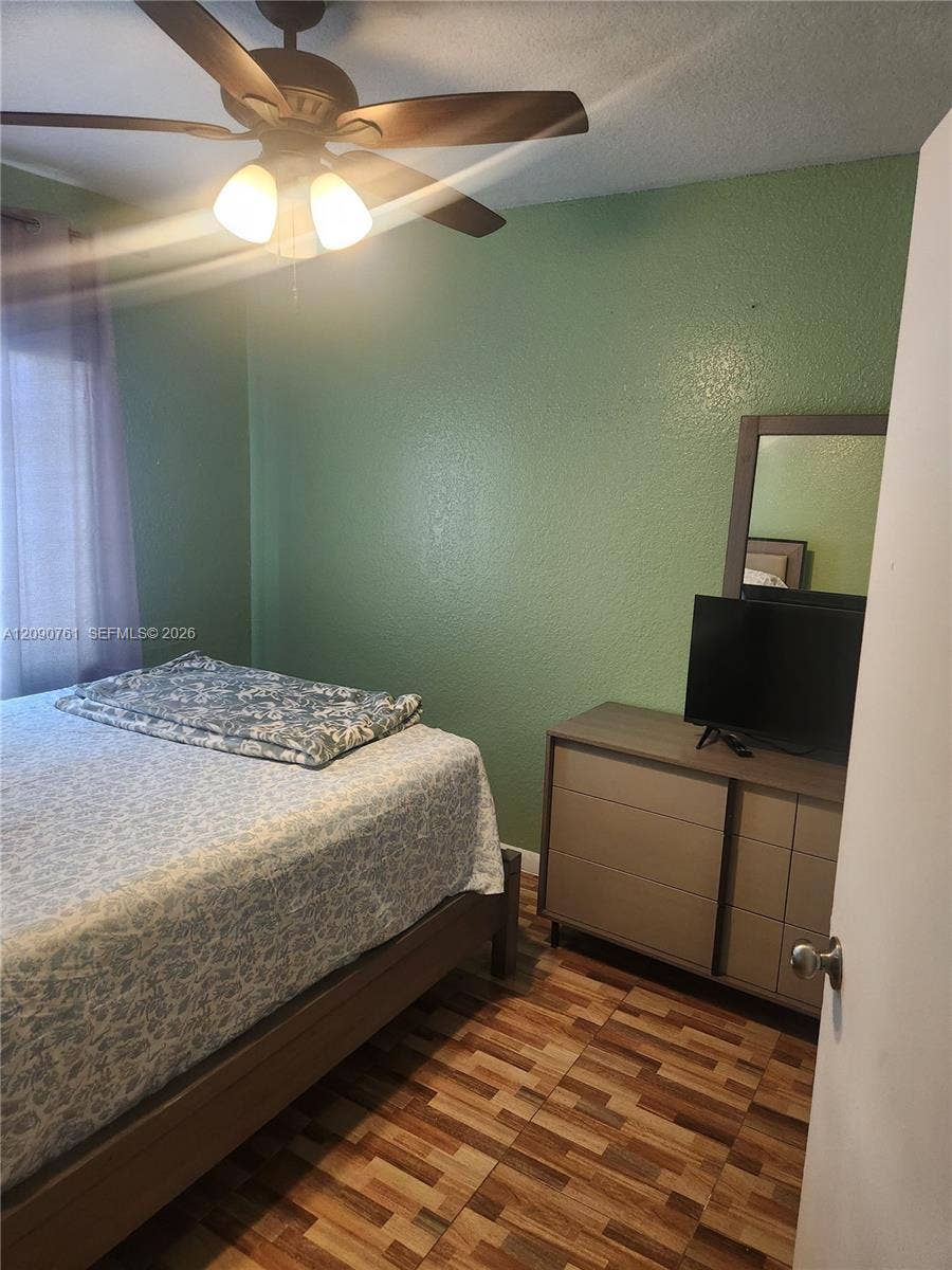 Room featuring wood-finish flooring, textured wall surfaces, and a ceiling fan with integrated lighting