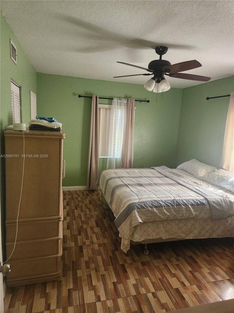 Room featuring wood-finish flooring, a multi-blade ceiling fan with integrated light fixture, and two windows with mounted curtain rods