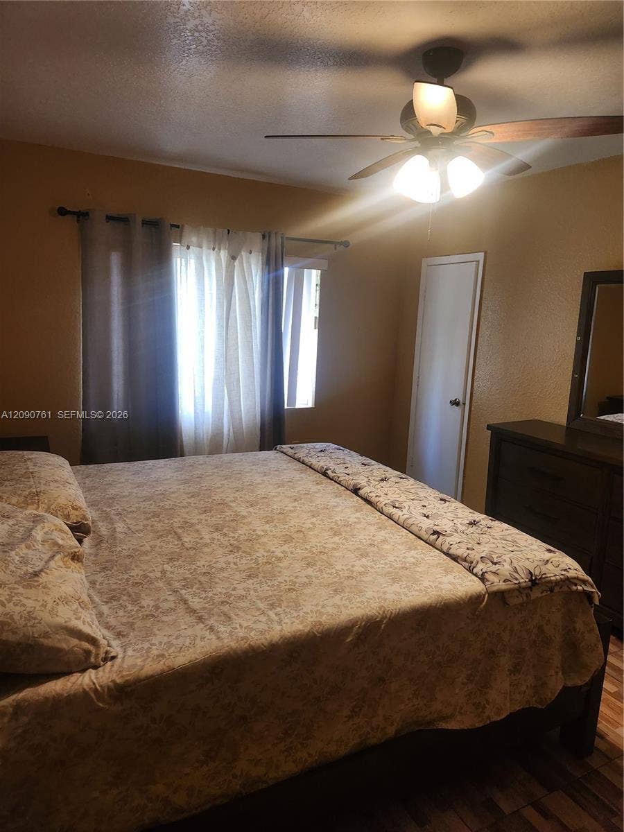 Room featuring wood-finish flooring, a ceiling fan with integrated lighting, and a single-panel interior door