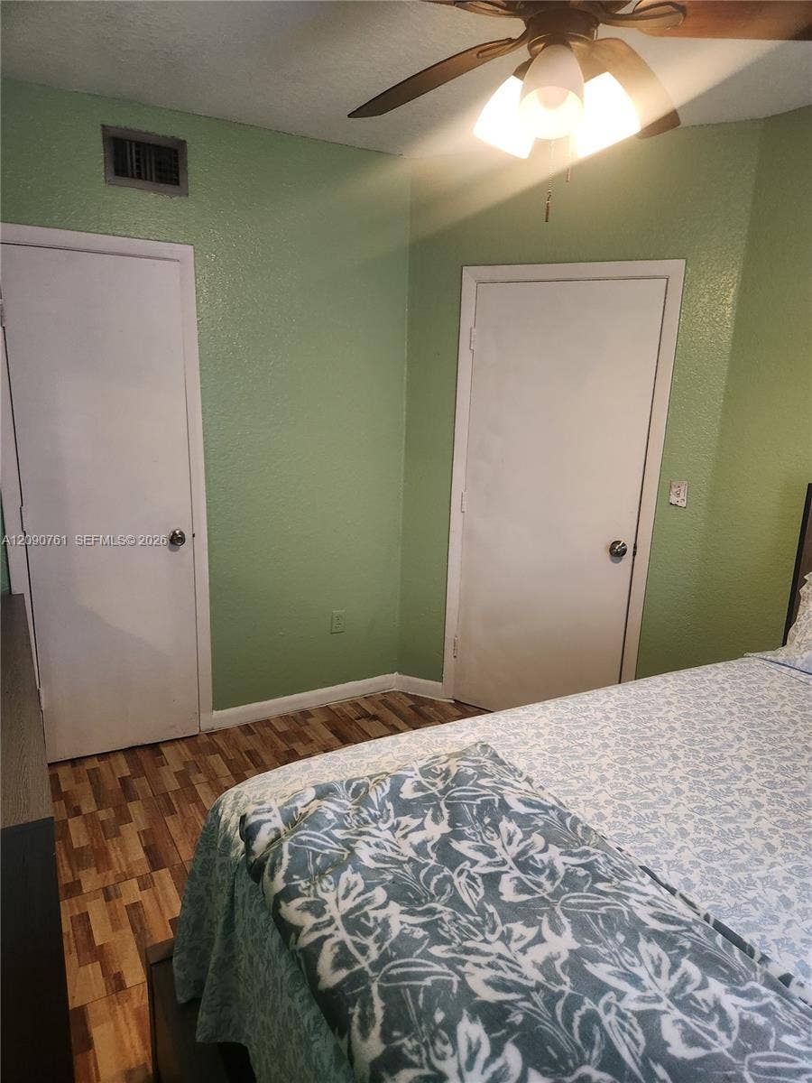 Room featuring wood-finish flooring, textured walls, and a ceiling-mounted light fixture with a fan