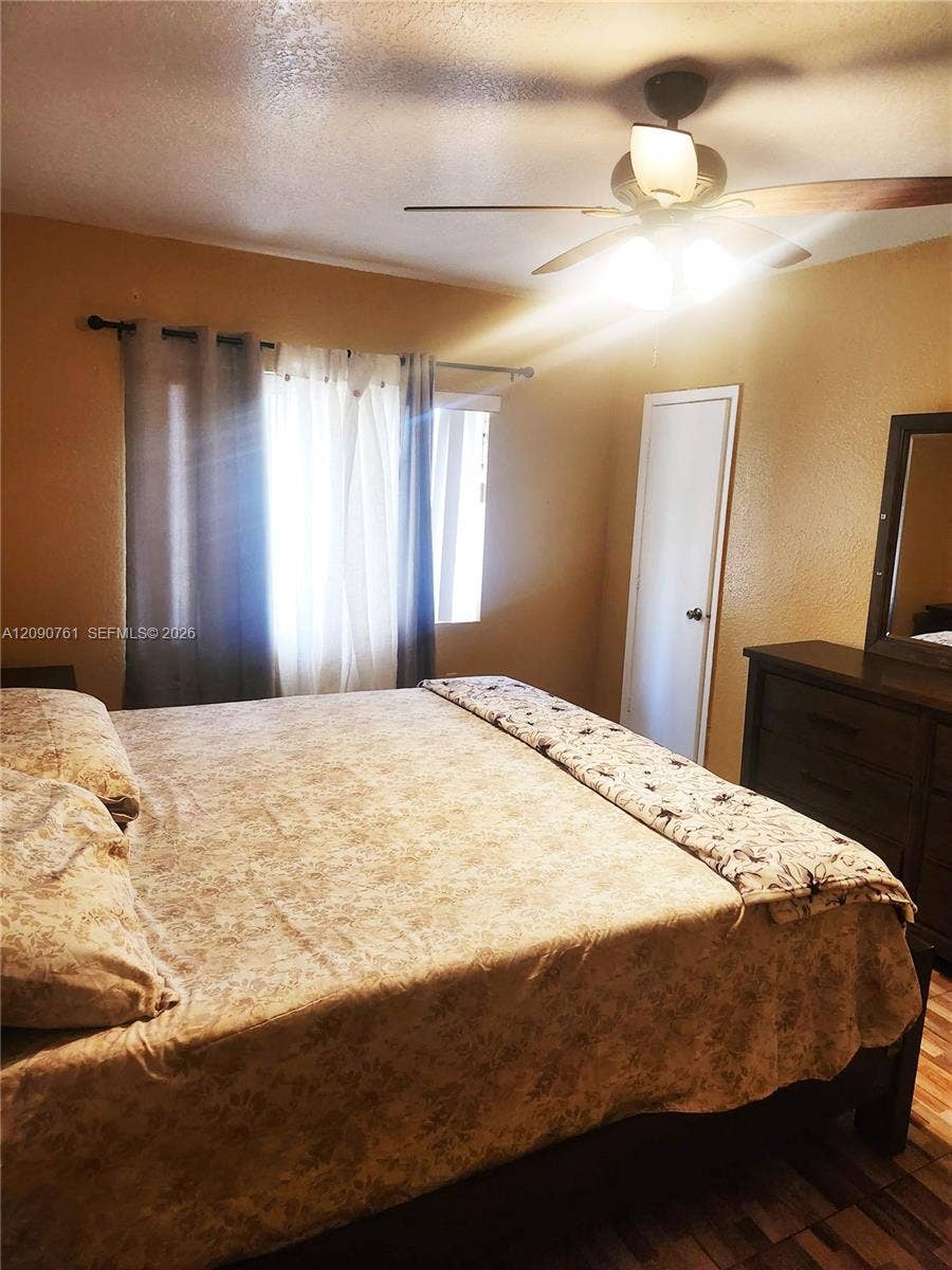 Room featuring wood-finish flooring, a ceiling fan with multi-light fixture, and a single-panel interior door