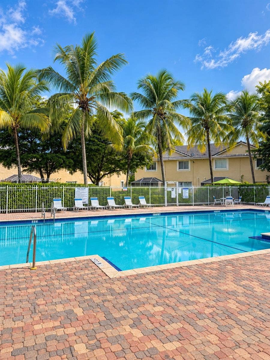 2196 Ensenada Terrace, Weston, FL 33327 Outdoor swimming pool with a paved brick deck, surrounded by palm trees and a perimeter fence