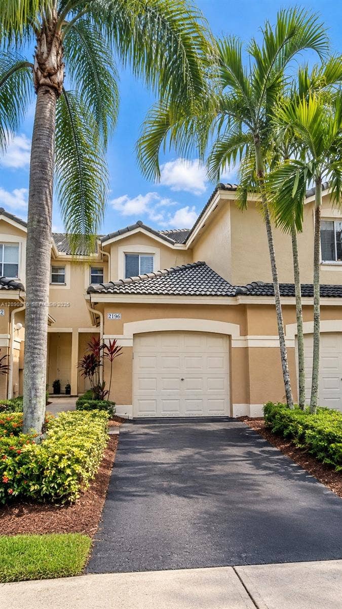 2196 Ensenada Terrace, Weston, FL 33327 Stucco exterior with a tiled roof, arched garage entry, paved driveway, and established landscape plantings