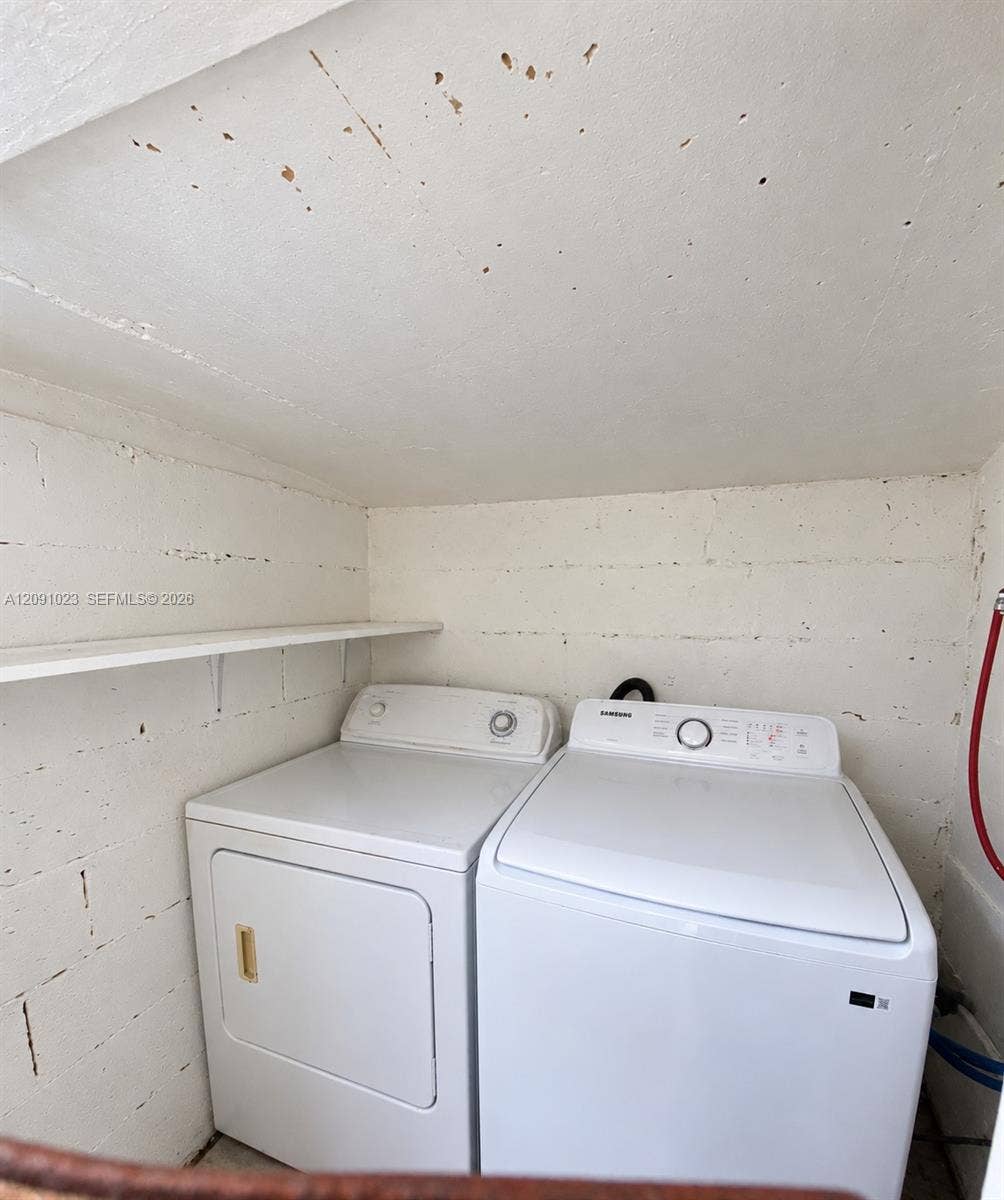 Laundry area featuring white top-load appliances and an integrated wall-mounted shelf against a painted masonry finish