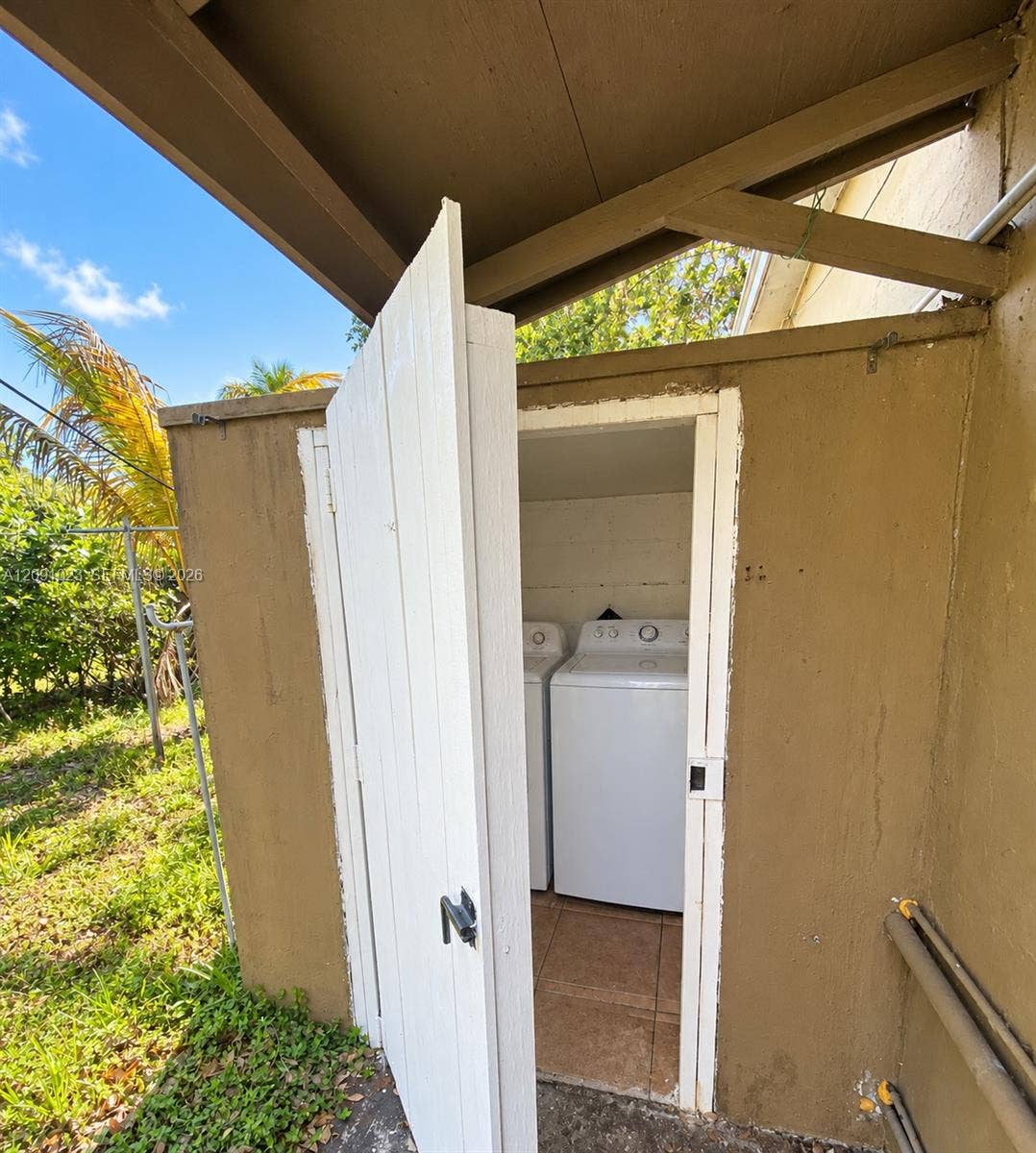 Exterior laundry enclosure featuring a solid-hinged door, tile flooring, and dedicated hookups for a washer and dryer