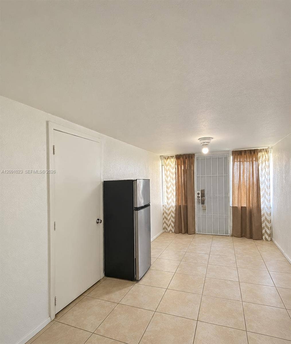 Neutral-toned tile flooring, metal security door, and overhead lighting fixture
