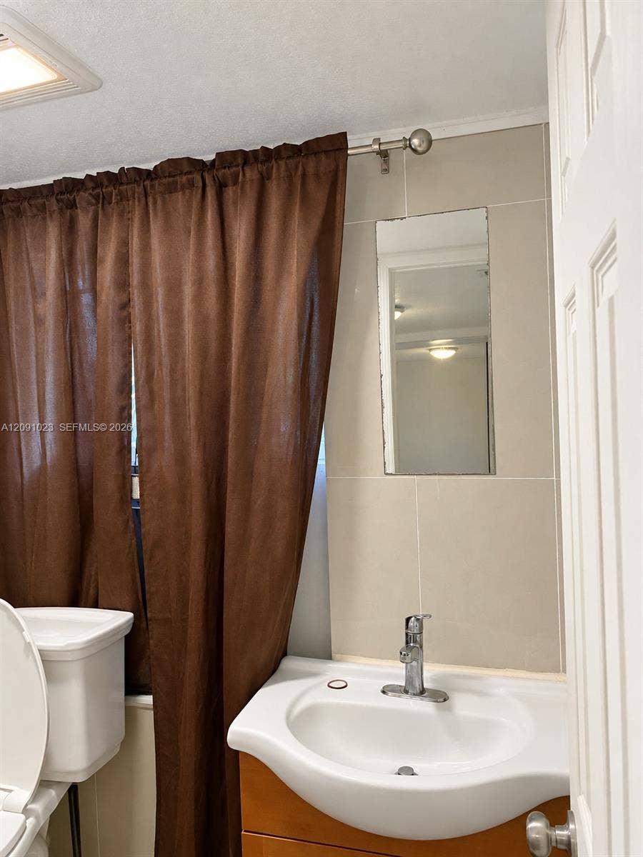 Wall-mounted rectangular mirror, ceramic sink basin with a single-handle chrome faucet, wood-finish cabinetry, and neutral-toned wall tiling