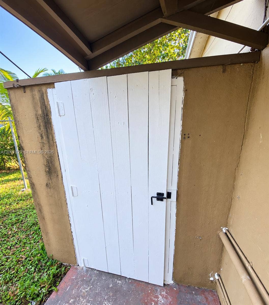 White vertical-plank gate with matte black hardware, integrated into a stucco-finished wall structure under a covered overhang