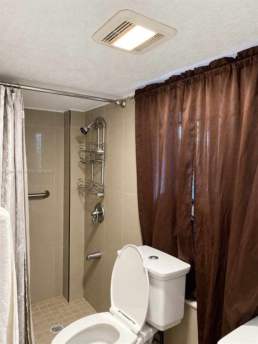 Full-height neutral wall tiling, integrated tub and shower combination with chrome fixtures, mosaic-tiled shower floor, and recessed ceiling lighting