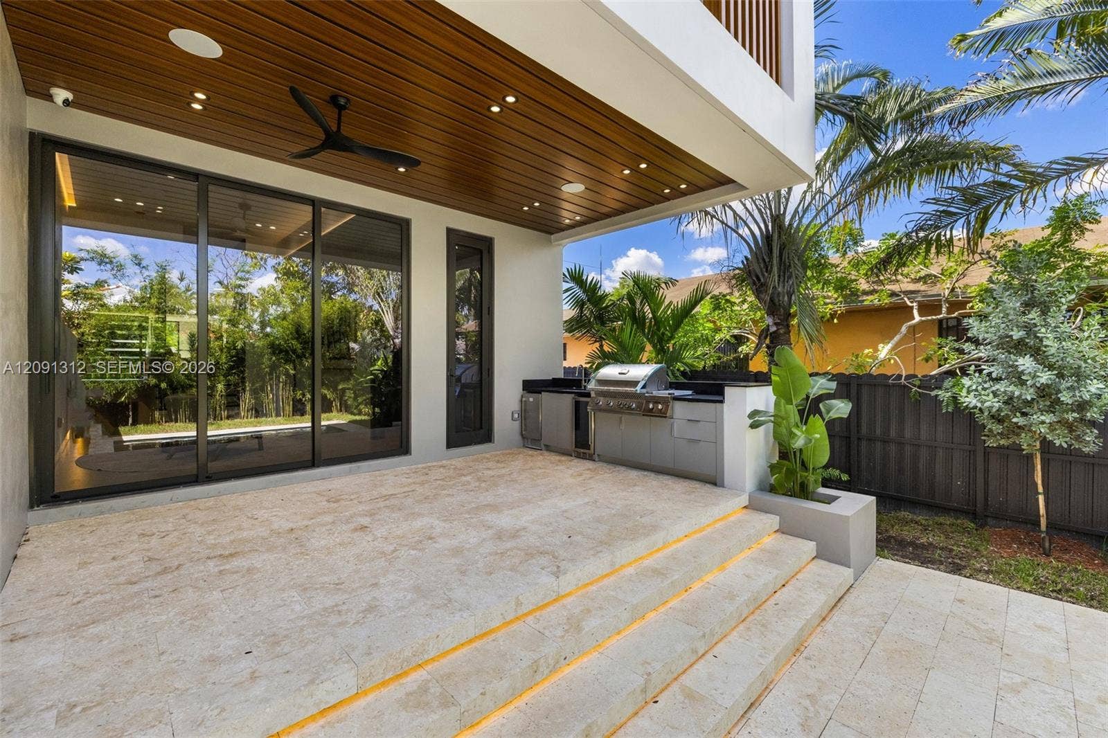 Covered patio featuring a wood-finished tongue-and-groove ceiling with recessed lighting, integrated outdoor kitchen with stainless steel grill, stone-tile flooring, and tiered staircase with step-level lighting