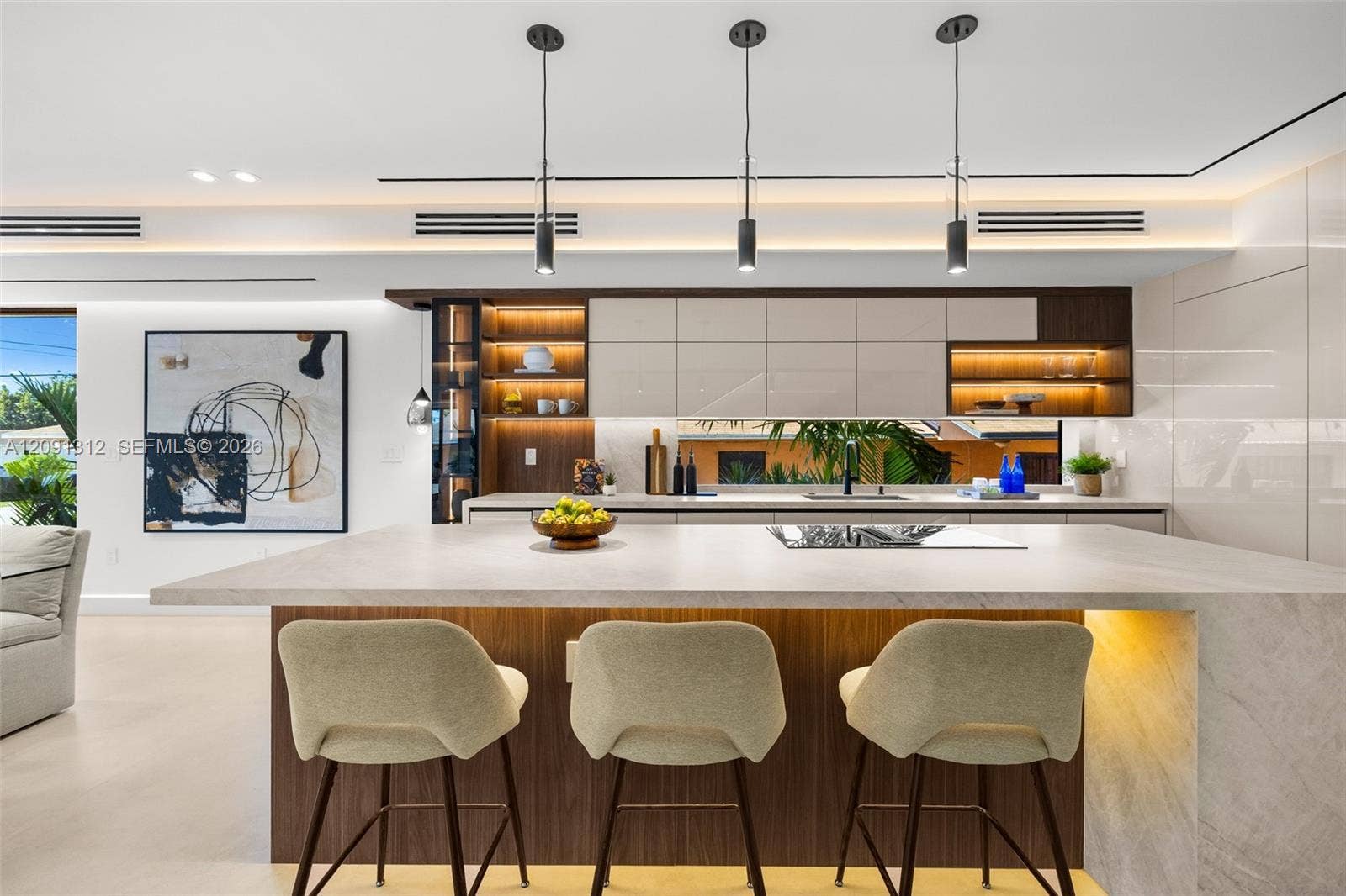 Kitchen featuring a large central island with stone-finish countertop, high-gloss cabinetry, linear pendant lighting, recessed accent shelving, and a horizontal backsplash window
