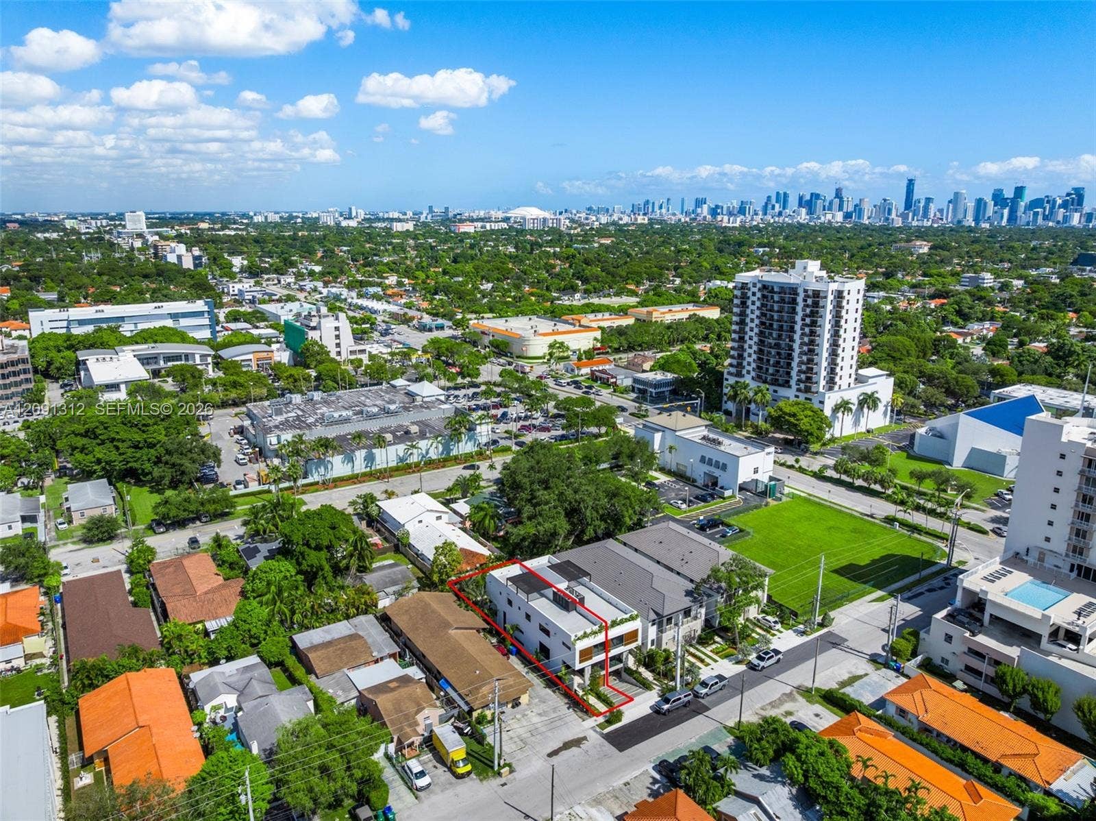 Aerial perspective of a multi-story residence featuring a flat roof with solar panels, a private rooftop deck, and balcony enclosures with horizontal slat privacy screening