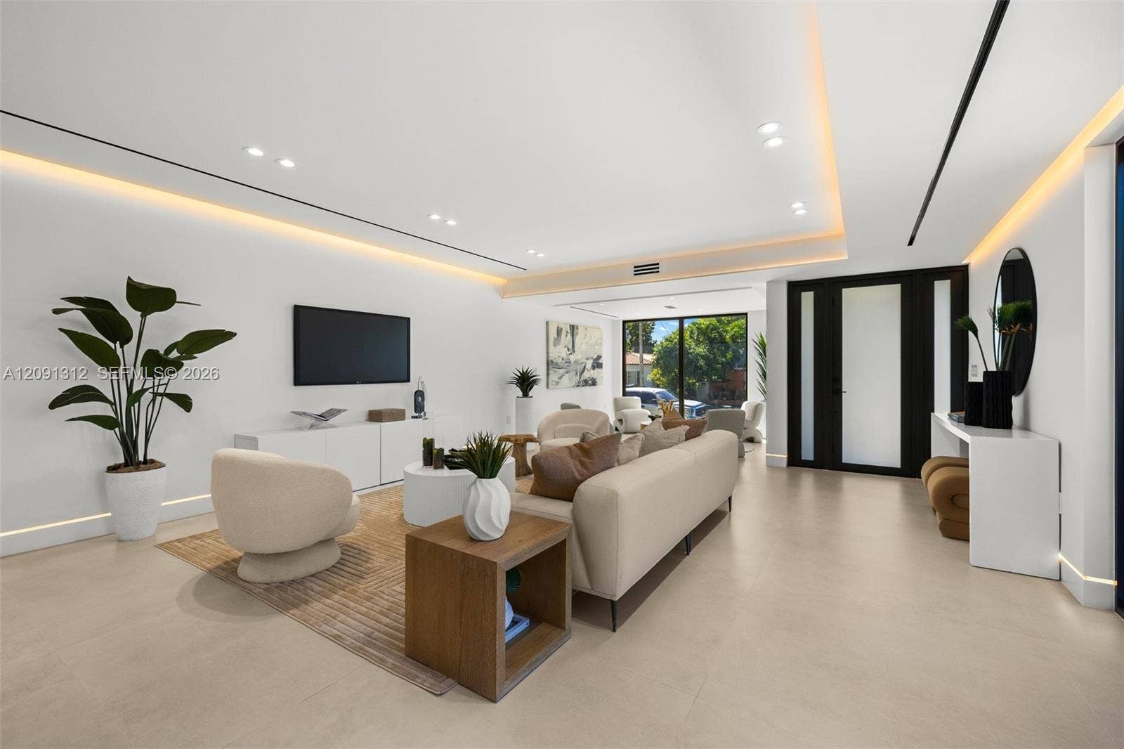 Modern living space featuring recessed ceiling lighting, cove LED accent lighting, smooth neutral-toned flooring, and a glass-paneled entry door with black frame