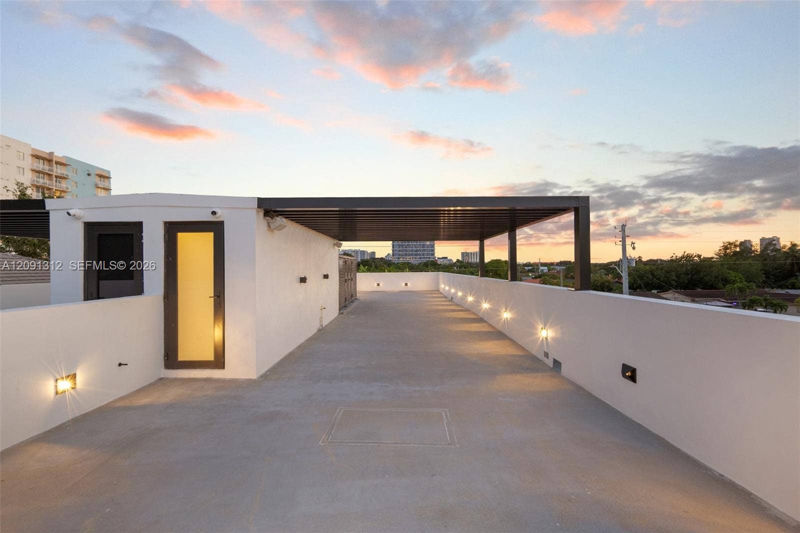 Rooftop terrace featuring smooth concrete flooring, solid perimeter walls, built-in wall-mounted lighting, and a metal-framed covered area