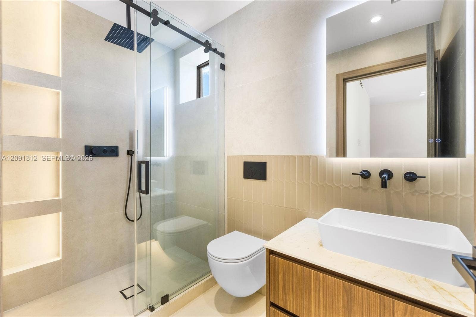 Modern bathroom featuring a wood-finish floating vanity, vessel sink with matte black wall-mounted faucet, wall-mounted toilet, and glass-enclosed shower with integrated recessed shelving