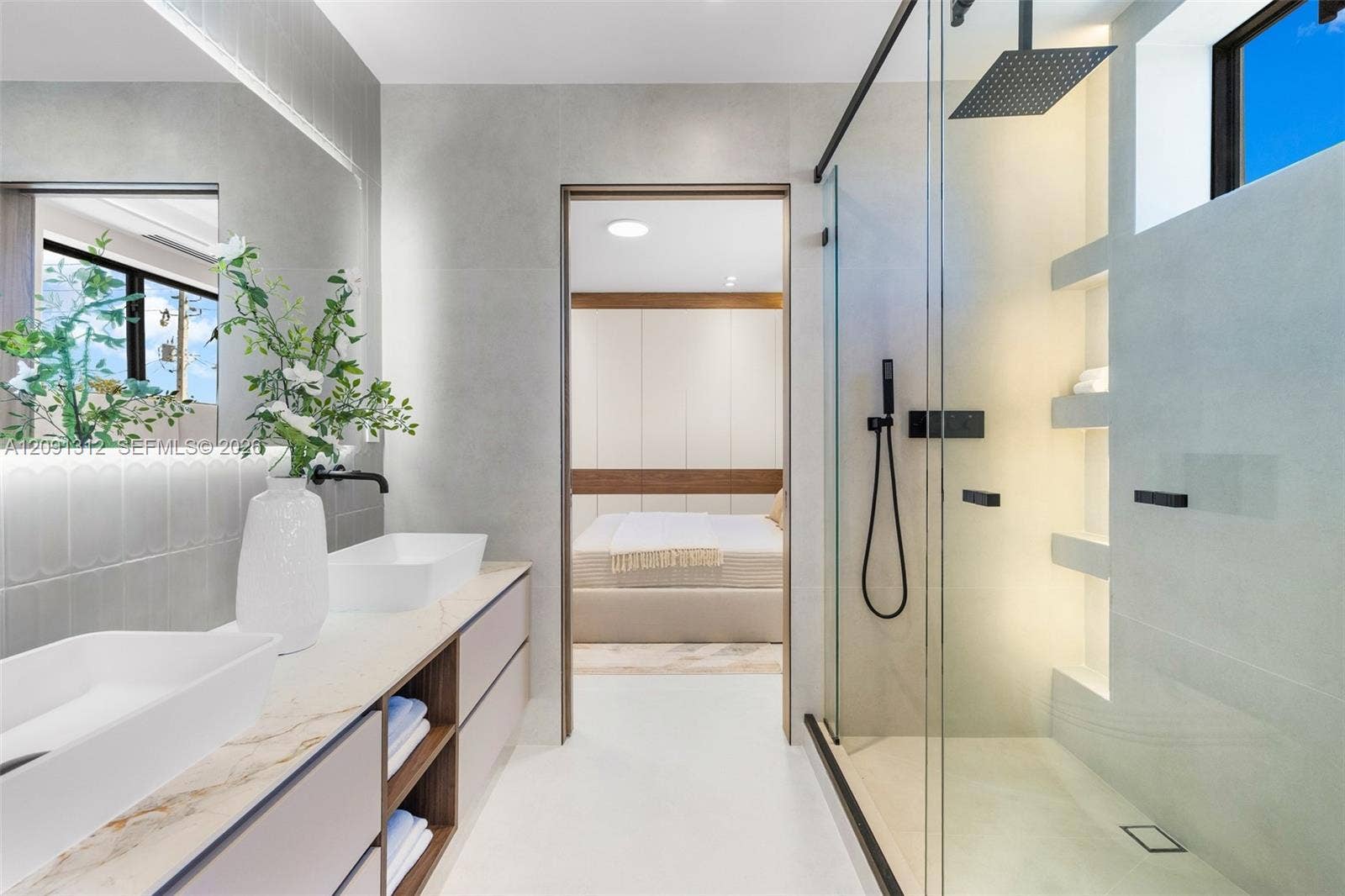 Floating dual vanity with stone-surfaced countertop, rectangular vessel sinks, matte black fixtures, walk-in glass-enclosed shower with built-in recessed shelving, and large-format wall tiling