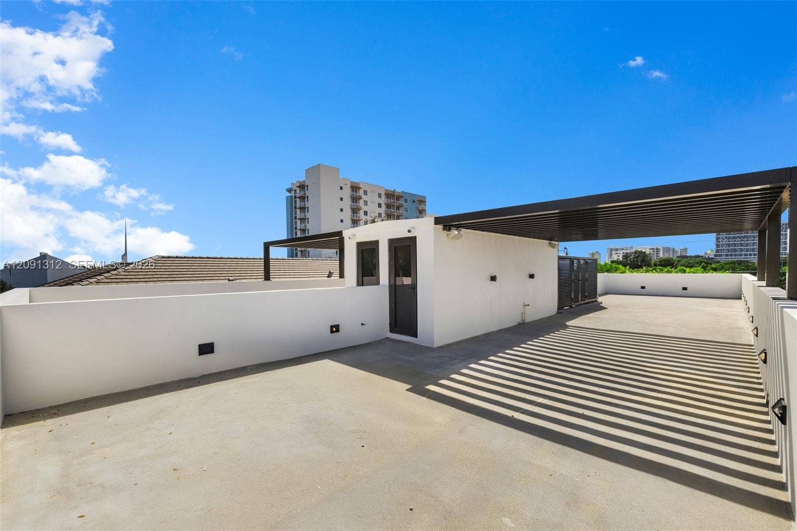 Rooftop terrace featuring concrete flooring, a partial louvered metal pergola, solid perimeter walls, and exterior wall-mounted lighting