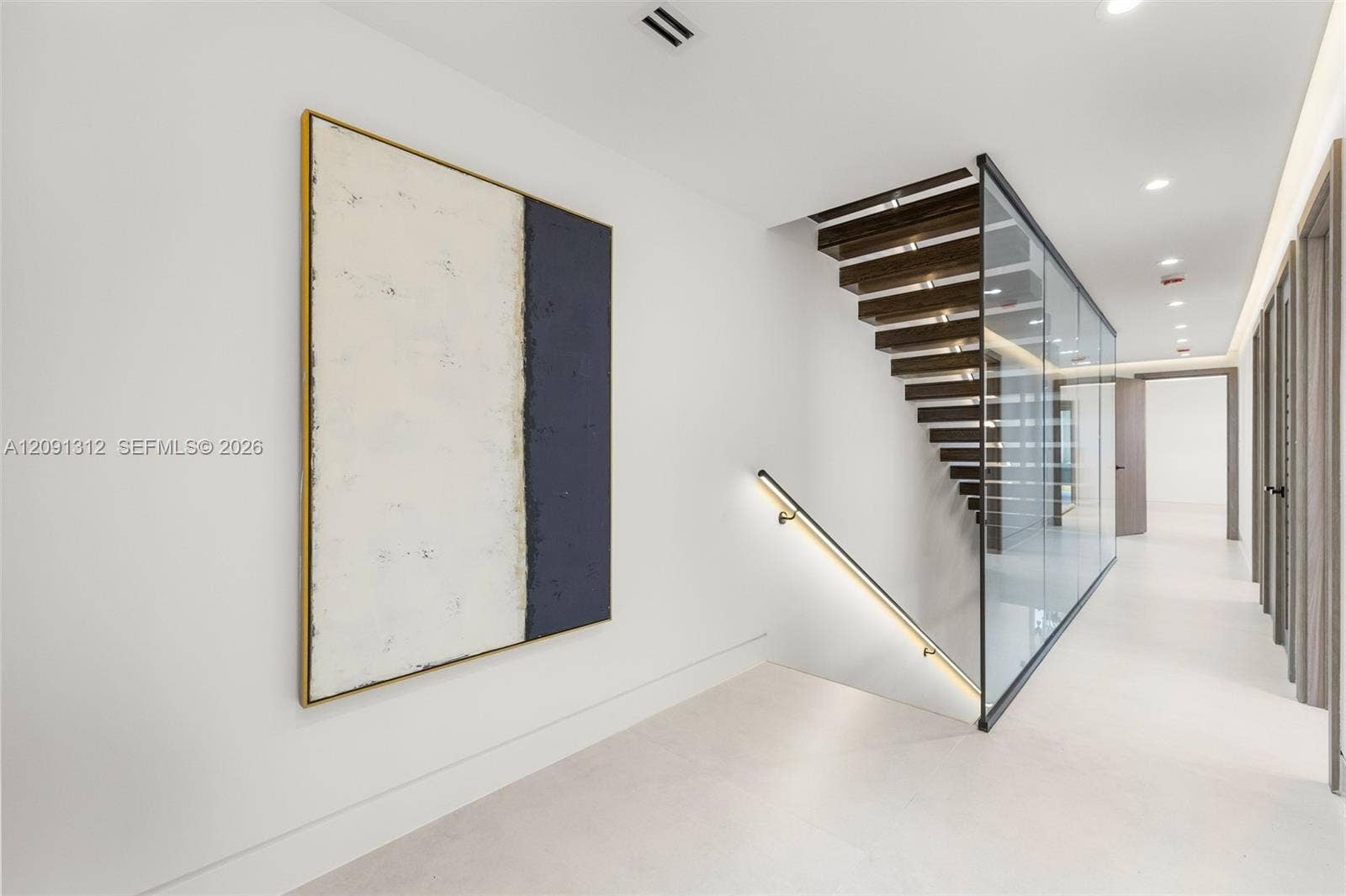 Staircase featuring open-riser wood treads, a full-height glass panel partition, a sleek wall-mounted handrail with integrated LED lighting, and large-format tile flooring