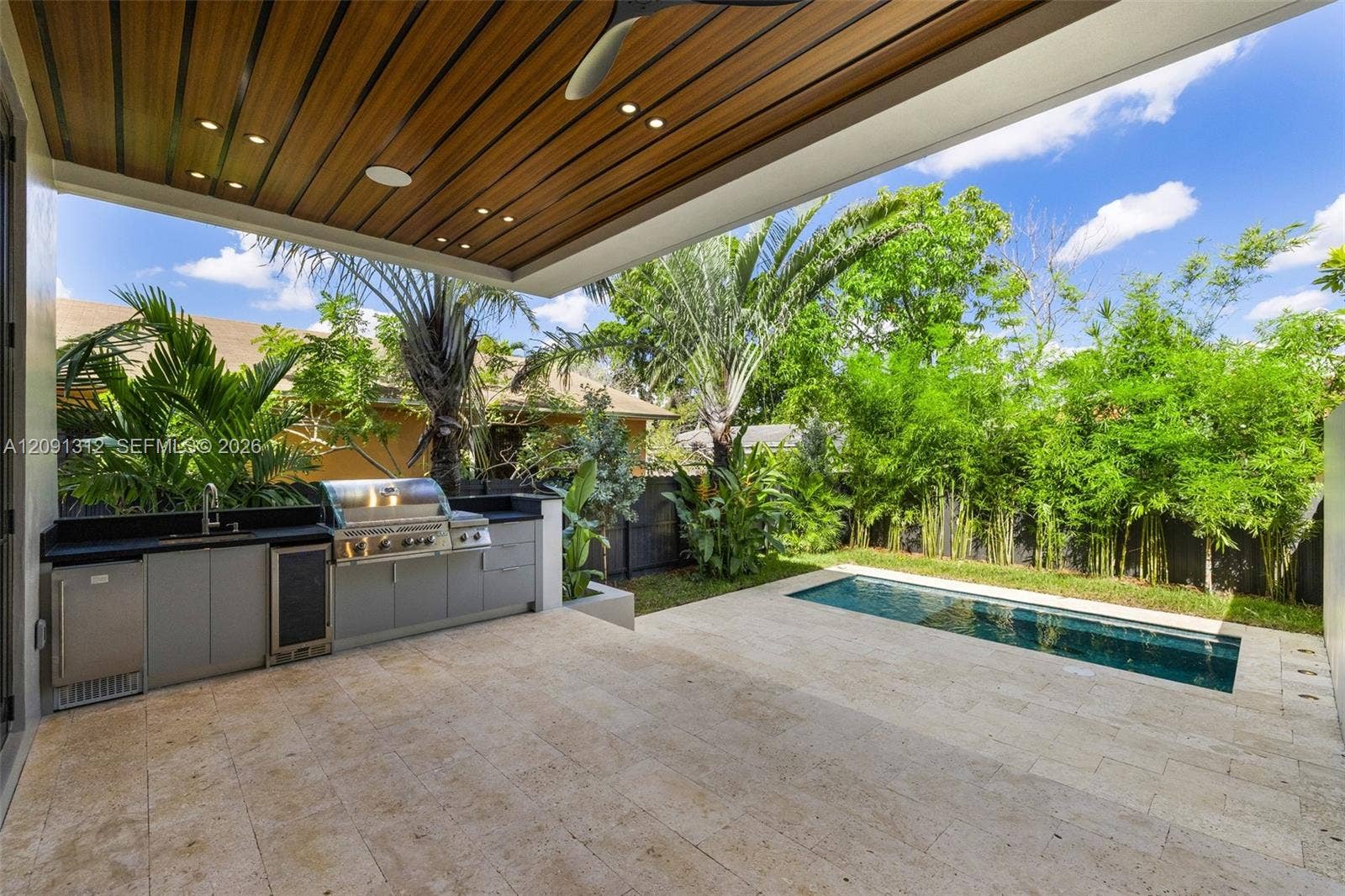 Covered outdoor kitchen featuring built-in cabinetry, stainless steel appliances, and a wood-slat ceiling with recessed lighting