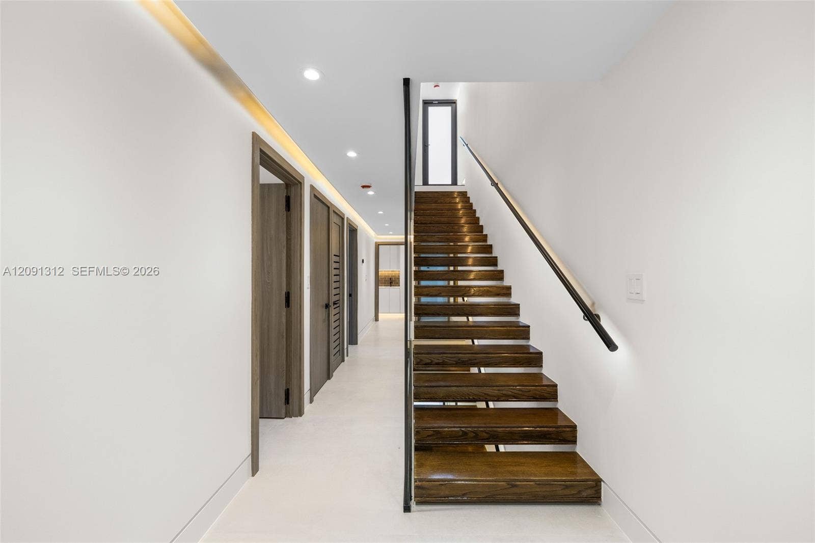 Open-tread staircase featuring wood-finish steps, a minimalist black metal handrail, recessed ceiling lighting, and smooth-finish flooring