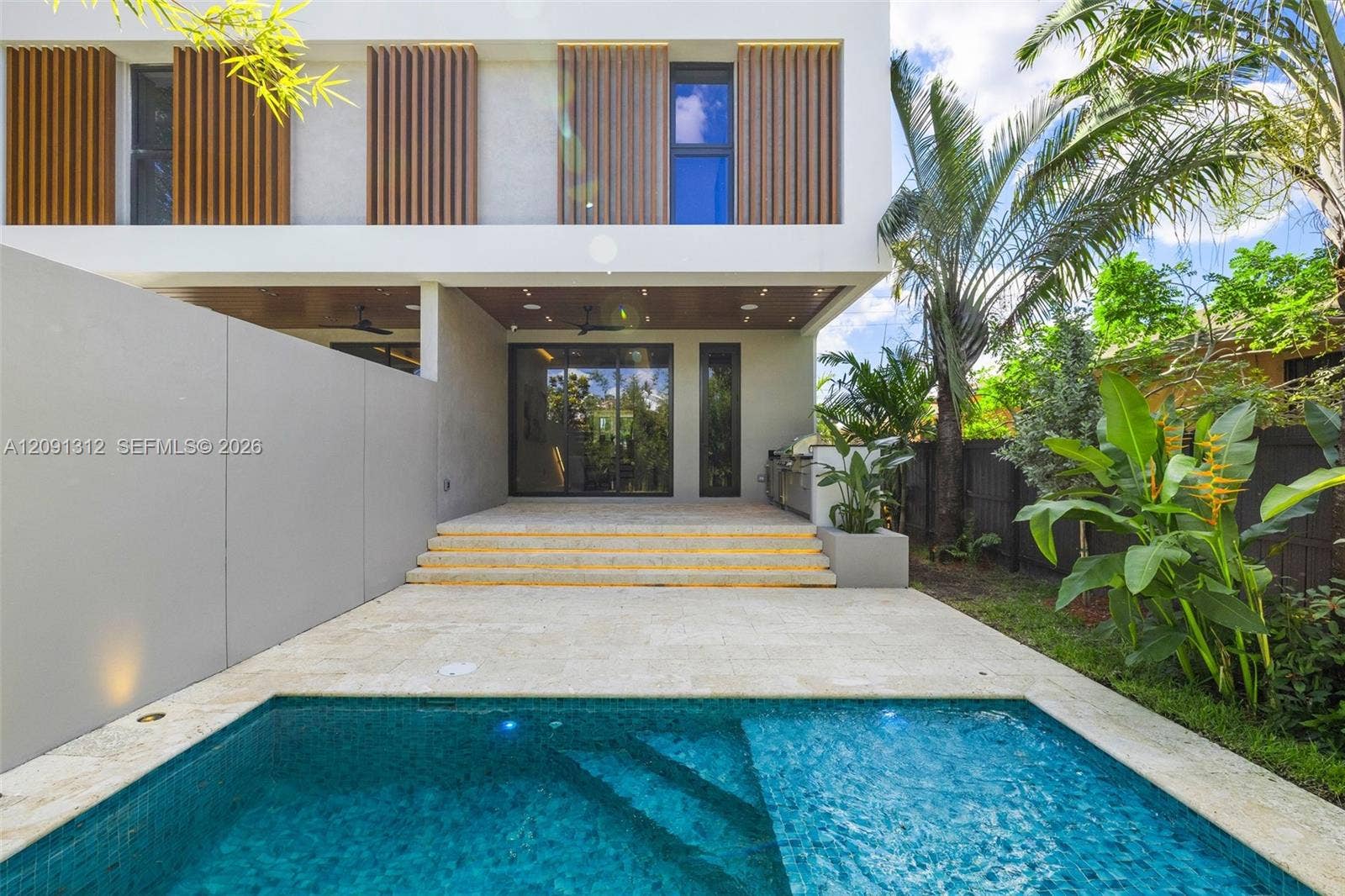Modern exterior featuring vertical wood-slat privacy screens, stone patio with tiered steps, built-in outdoor kitchen, and a tiled swimming pool