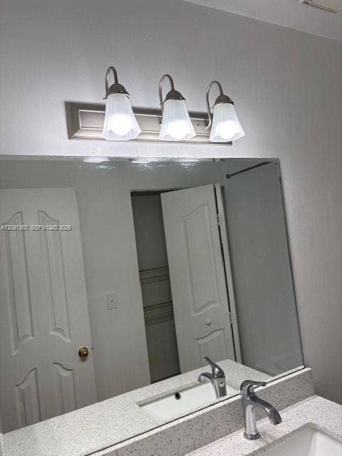18356 NW 68th Avenue, #E, Hialeah, Hialeah, FL 33015 Large wall-mounted mirror above a vanity with stone-flecked countertop, undermount sink, metallic faucet, and a three-light fixture with fluted glass shades