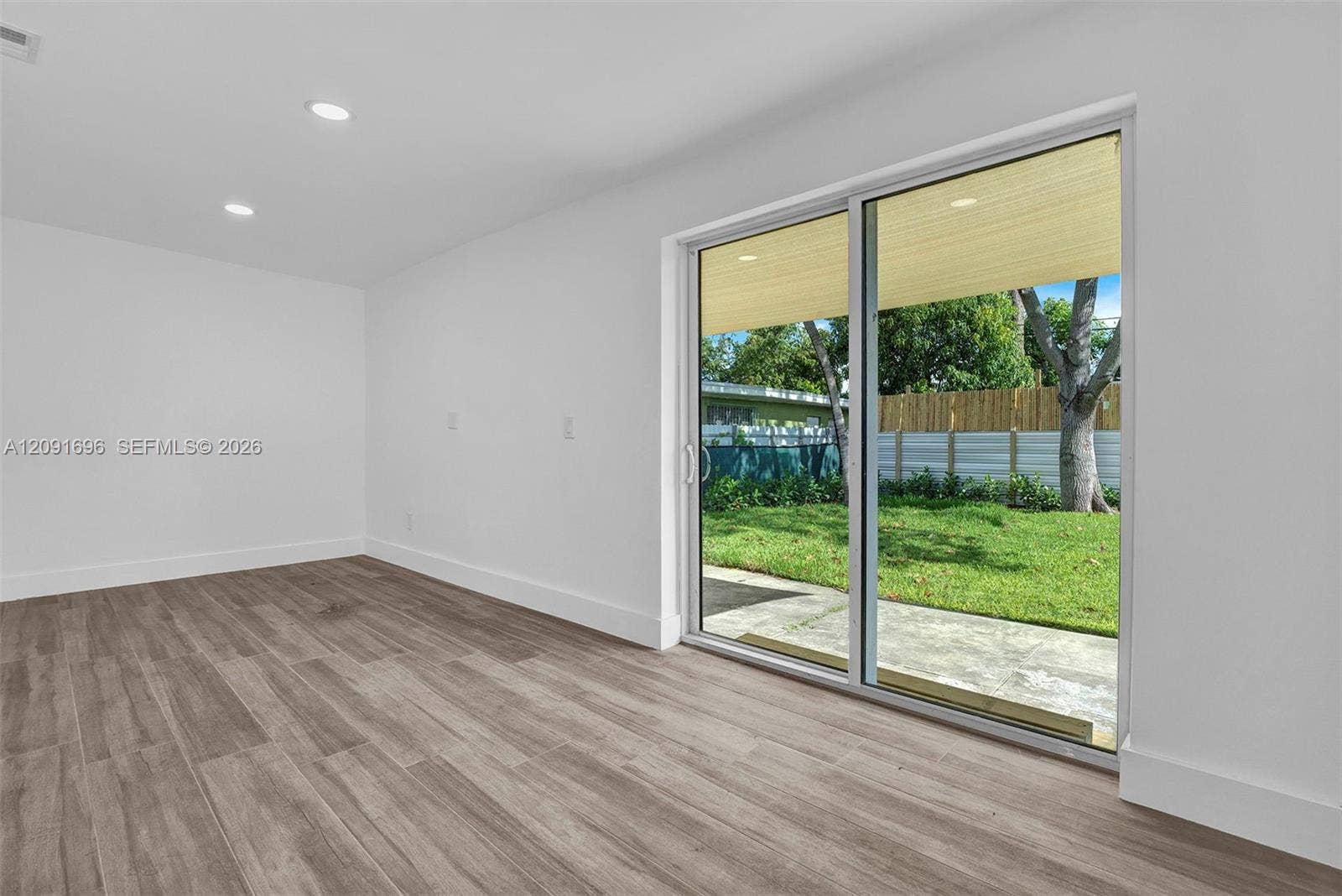 Interior space featuring wood-finish flooring, recessed lighting, and large sliding glass doors opening to a concrete patio, grassy yard, and wood fencing