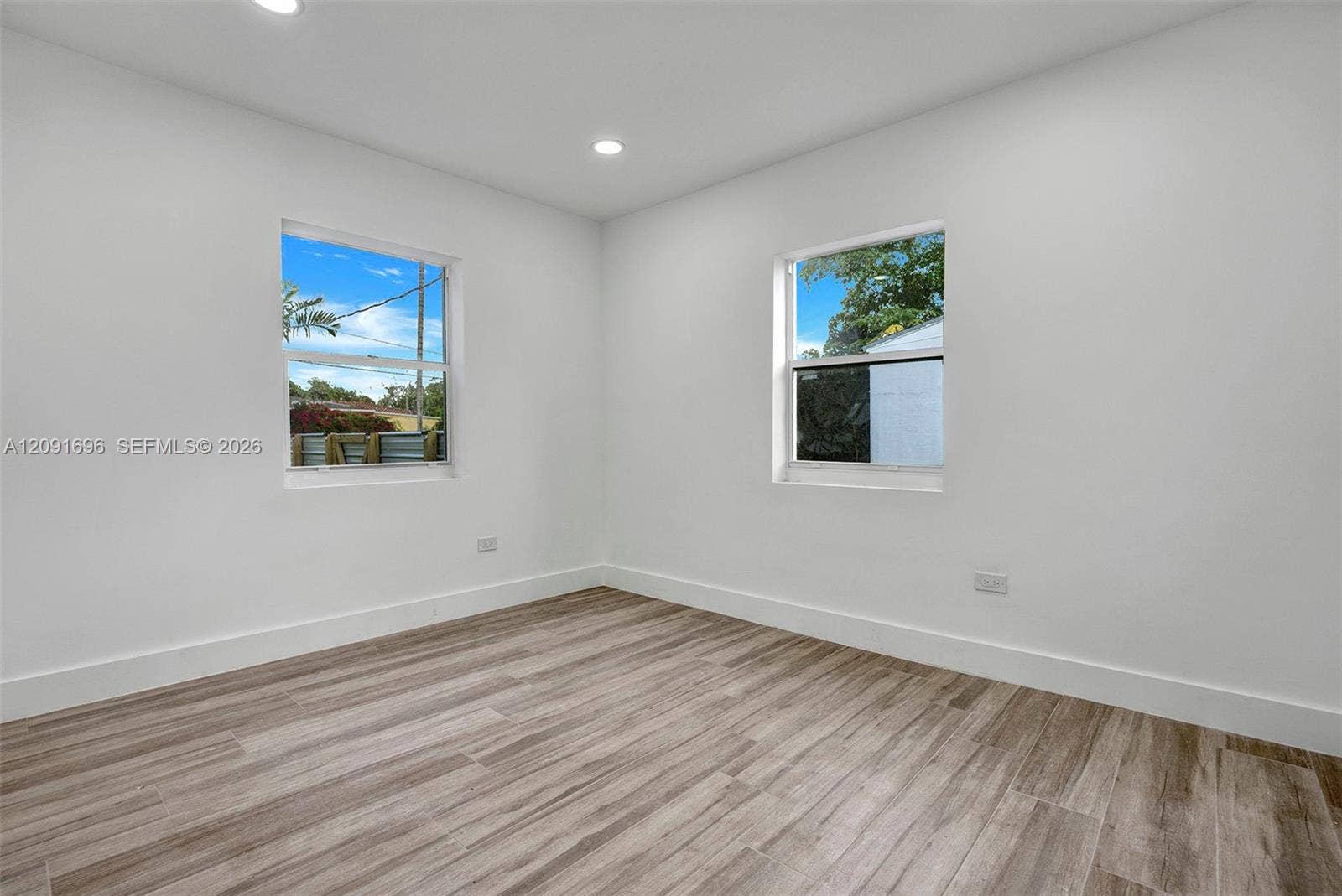 Neutral-toned interior room featuring wood-finish flooring, white walls, and recessed lighting with dual windows