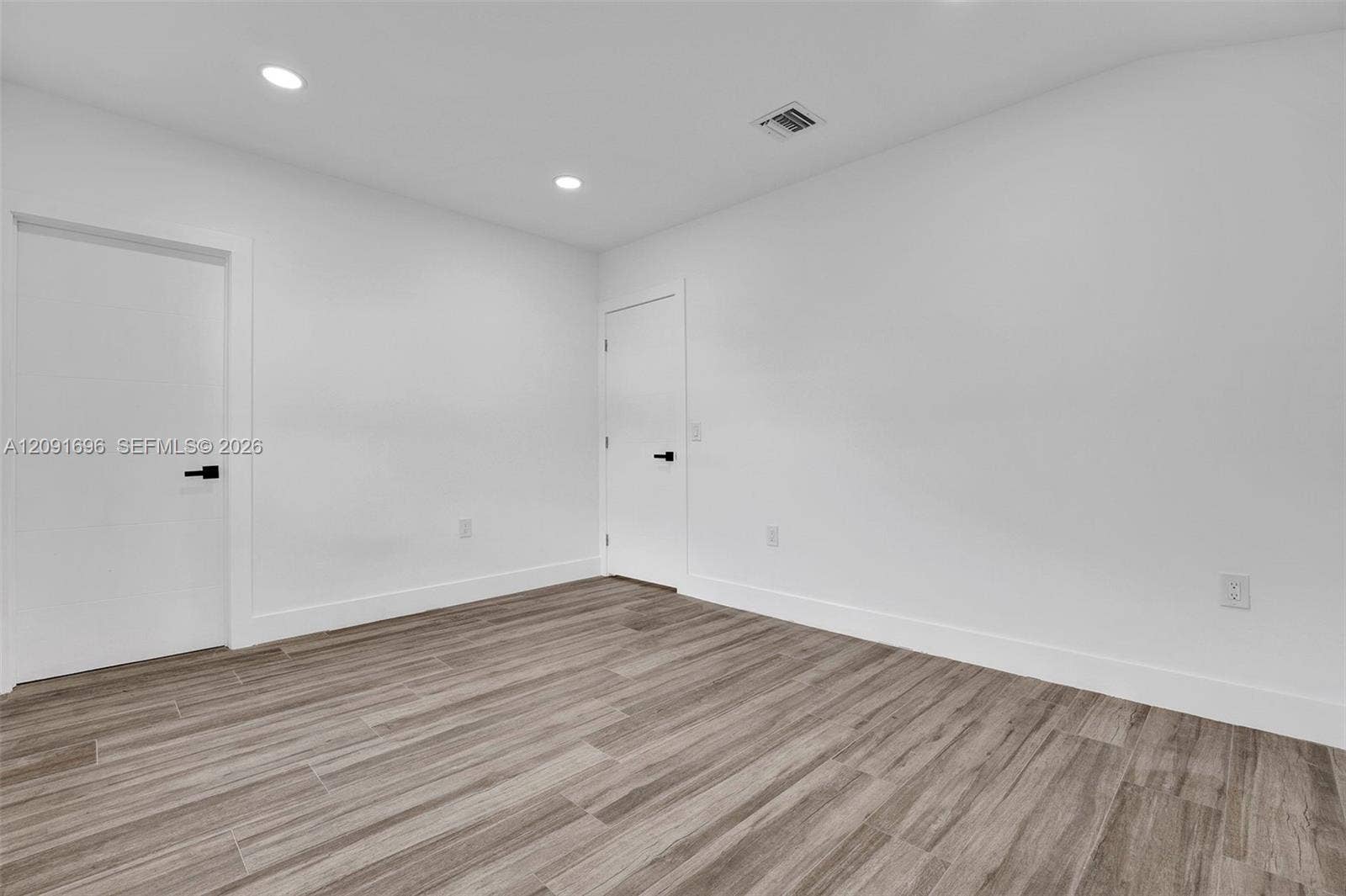 Interior space featuring wood-finish flooring, neutral white walls, recessed ceiling lighting, and solid-core doors with matte black hardware