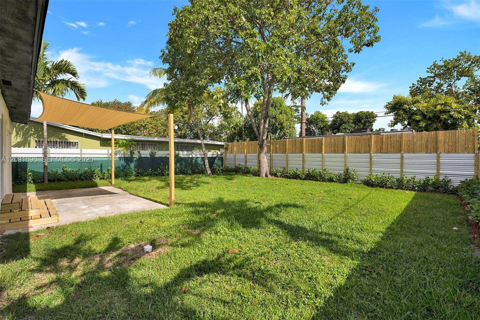 Fenced backyard featuring a manicured lawn, concrete patio with overhead shade canopy, and mature trees