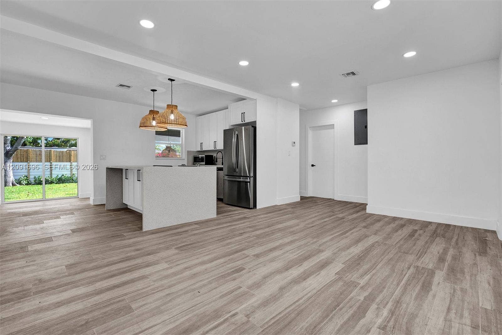 Open-concept interior featuring wood-finish flooring, recessed lighting, white cabinetry, a kitchen island with quartz-style waterfall countertop, and stainless steel appliances