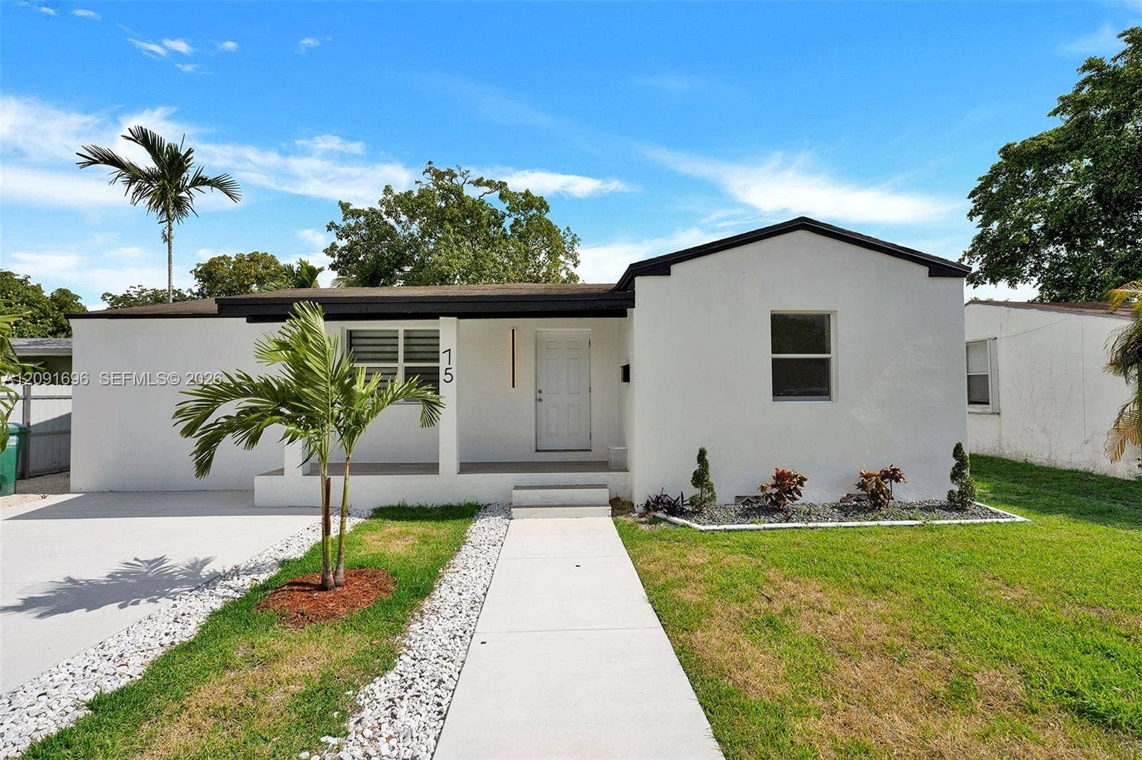 Single-story exterior featuring white smooth-stucco siding, a covered entryway, a concrete walkway, and landscaped garden beds with stone accents
