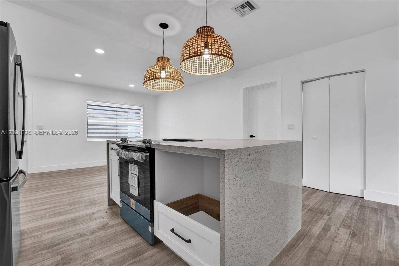 Kitchen featuring an island with a stone-finish countertop, dual woven pendant lights, stainless steel slide-in range, and wood-finish flooring throughout