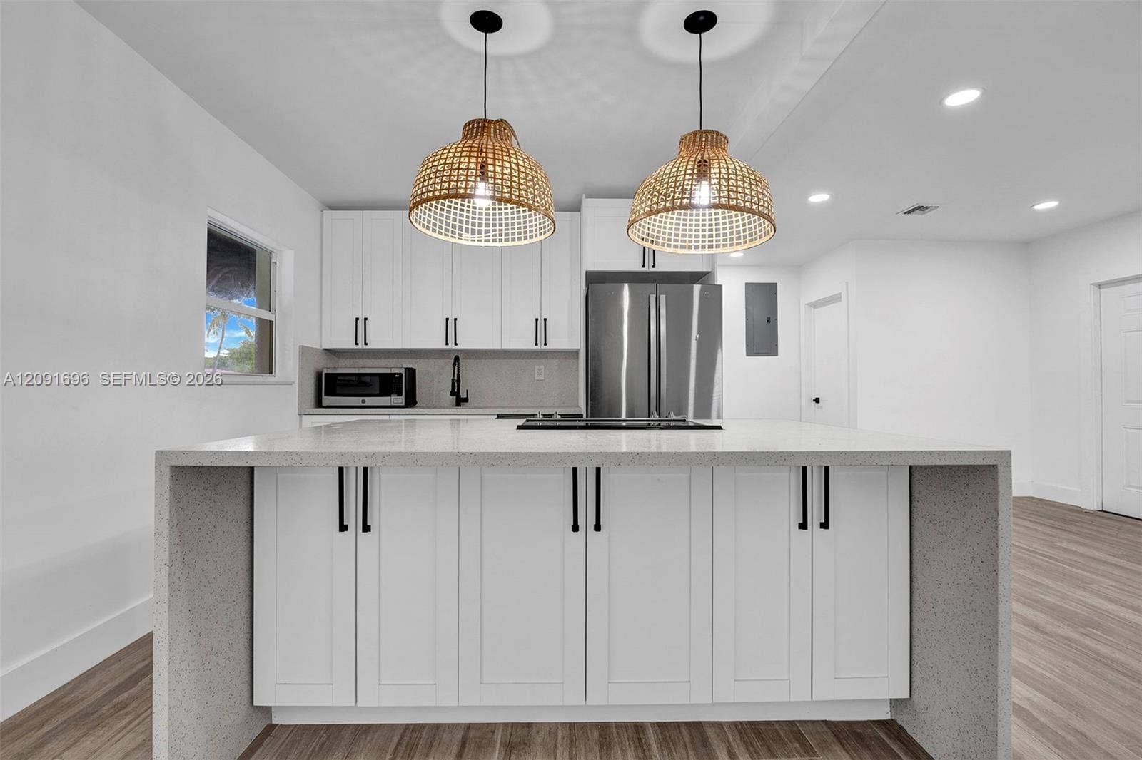 Kitchen featuring white shaker-style cabinetry, quartz countertop waterfall island, stainless steel appliances, and woven pendant lighting over wood-finish flooring