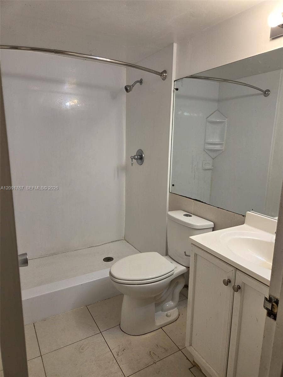 9101 W Sample Road, #102, Coral Springs, FL 33065 Bathroom featuring a walk-in shower with integrated shelving, white cabinetry, a single-basin vanity, and large-format tile flooring