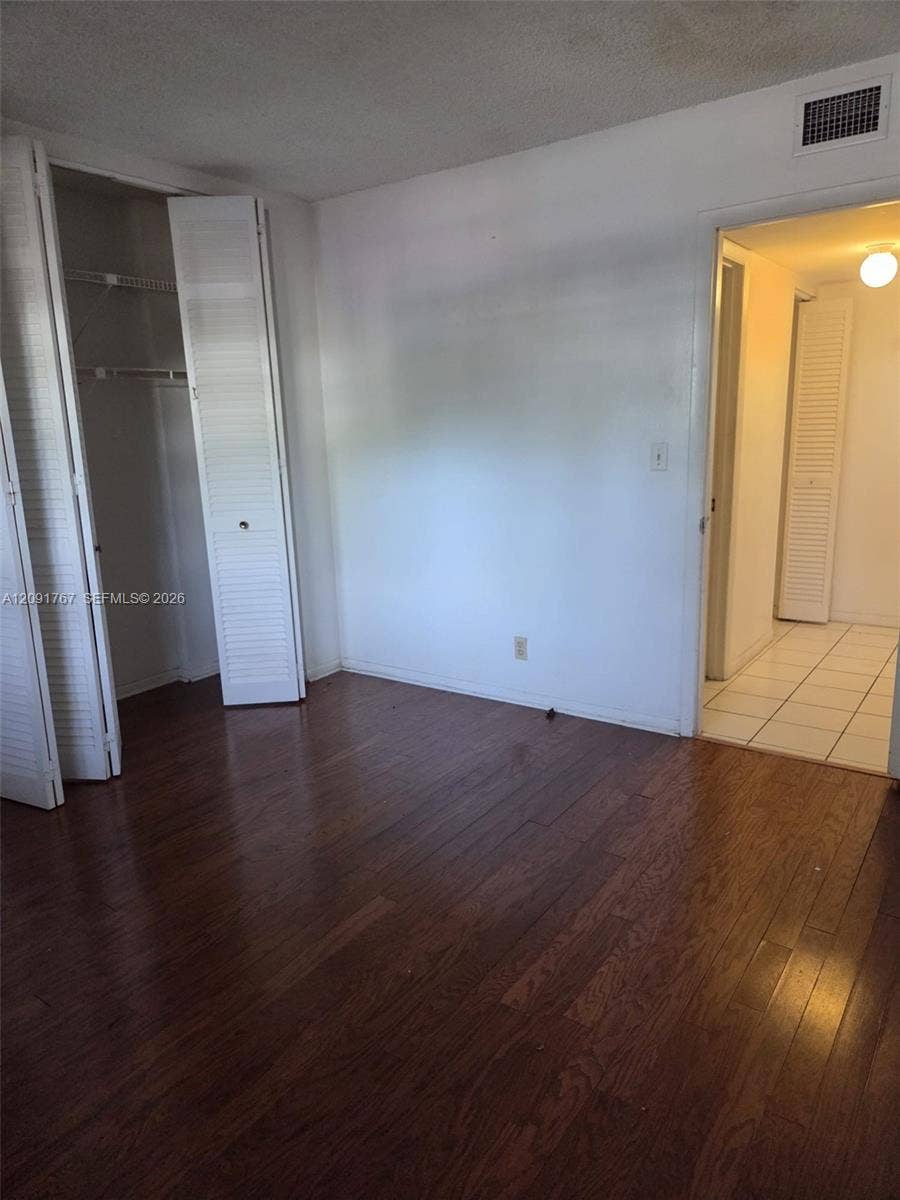 9101 W Sample Road, #102, Coral Springs, FL 33065 Room featuring dark wood-finish flooring, a built-in closet with louvered bifold doors, and a doorway opening to a tiled area