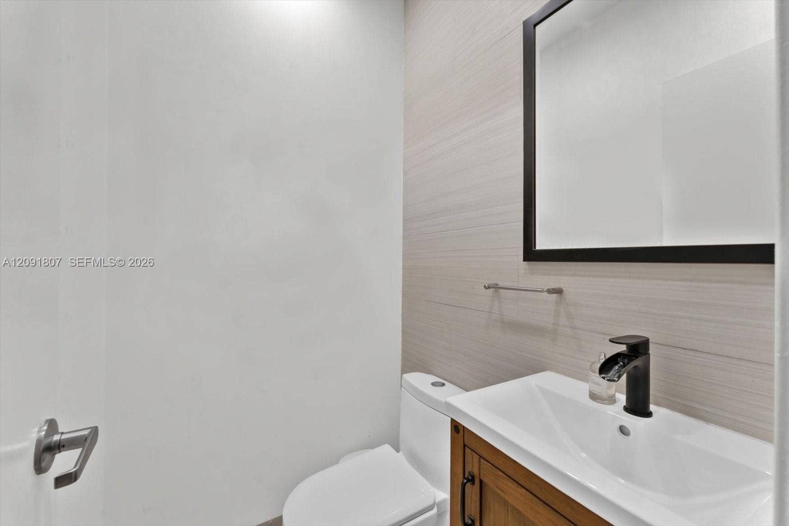 Vanity with a wooden cabinet base and integrated rectangular basin, matte black faucet, framed mirror, and textured tile wall accents