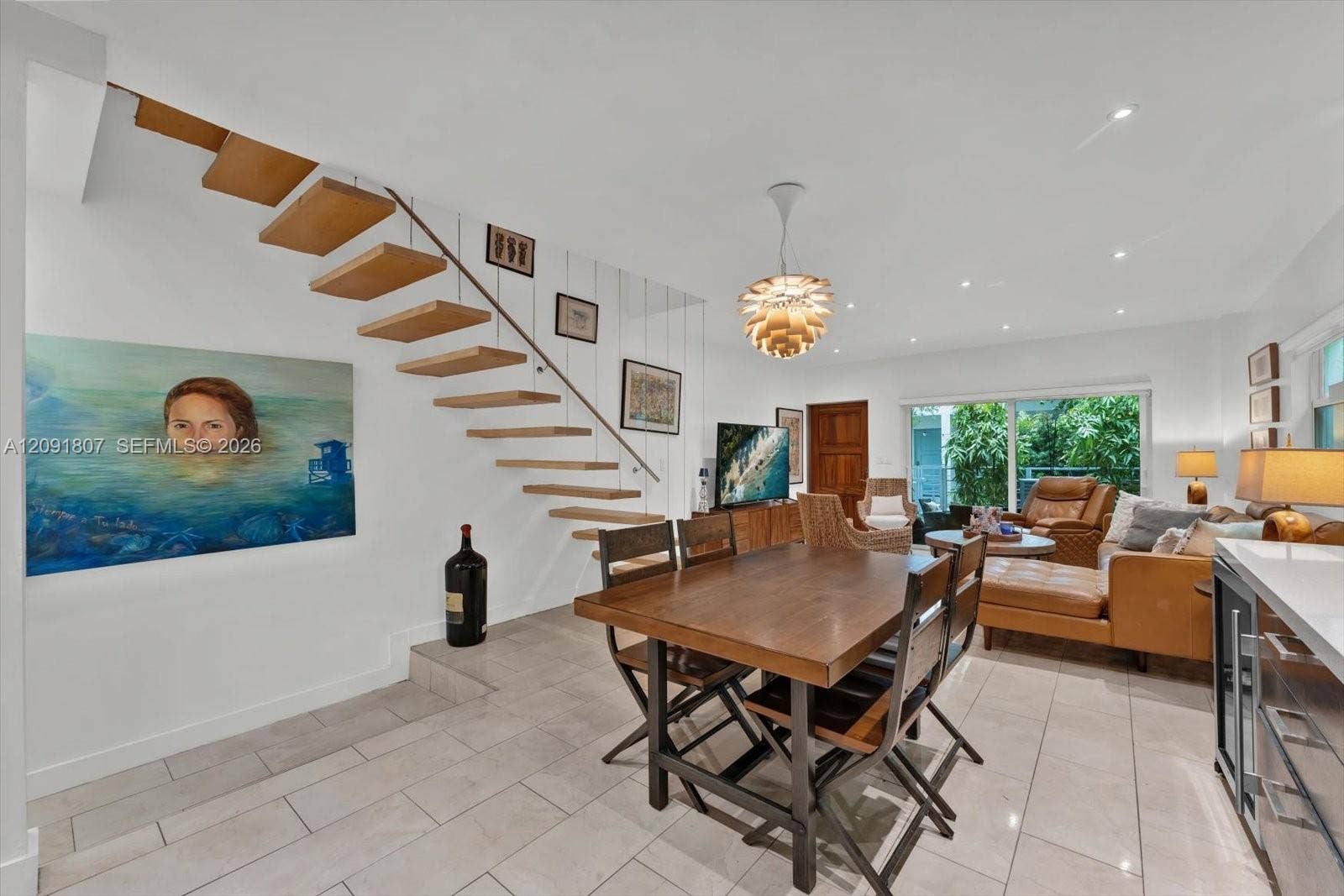 Open-concept area featuring a floating staircase with wood treads, light-toned ceramic tile flooring, recessed lighting, a modern spherical pendant light fixture, and large sliding glass doors